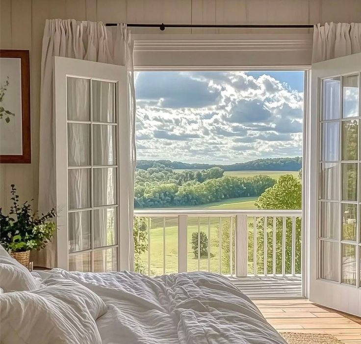 Bedroom with open French doors revealing a sunny countryside view, enhancing a serene and relaxing atmosphere.