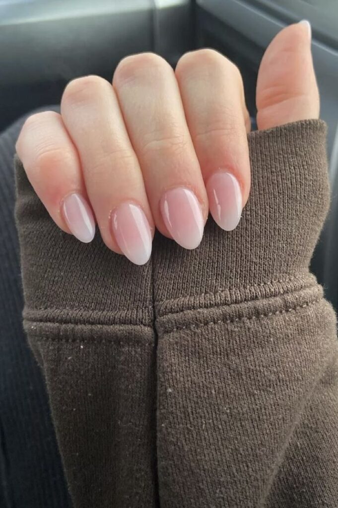 Close-up of hand with natural, glossy nude nails and brown sweater sleeve.