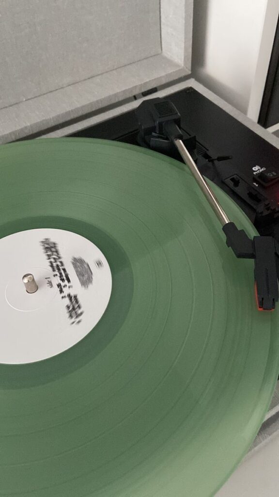 Green vinyl record playing on a turntable with a tonearm.
