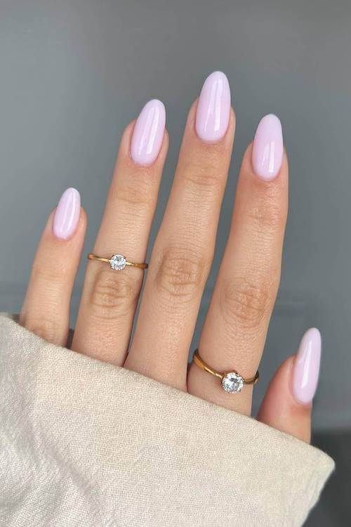 Close-up of a hand with pastel pink almond-shaped nails, wearing two gold rings with gemstones.