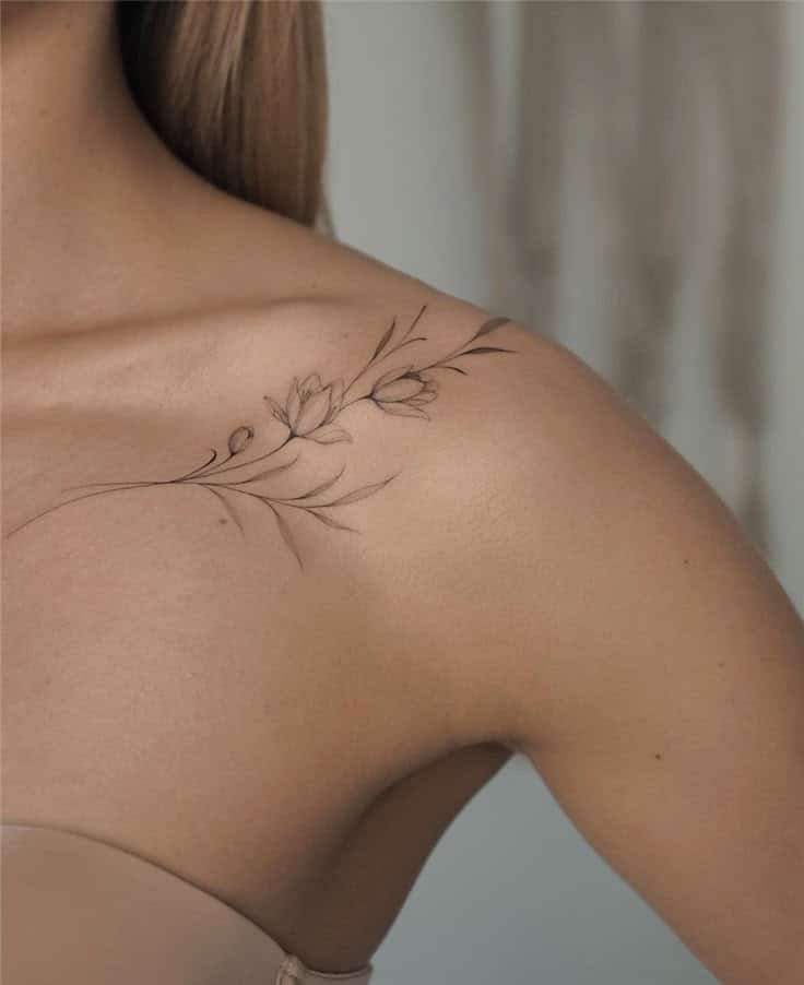 Delicate floral tattoo on a woman's shoulder, featuring thin line art of blossoms and leaves.