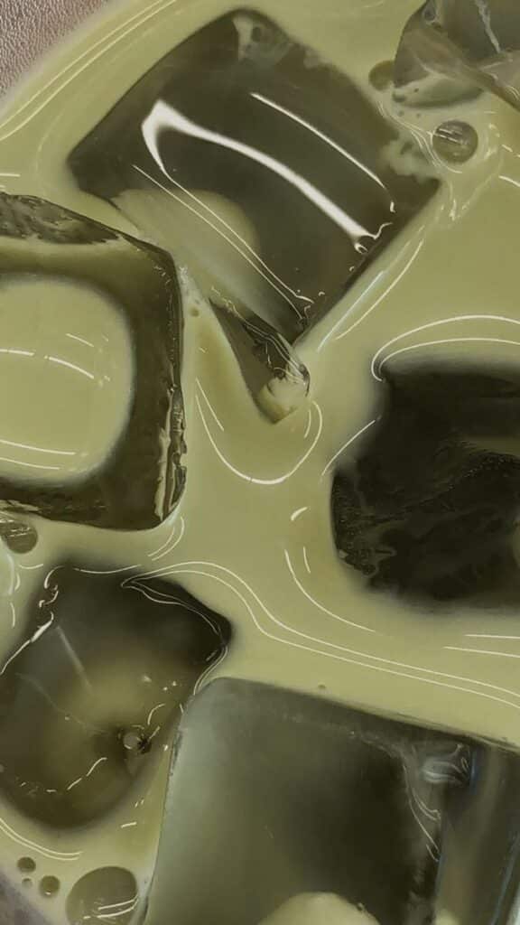 Close-up of iced matcha latte with swirling patterns and glossy ice cubes. Refreshing summer drink. iPhone Green Aesthetic Wallpaper