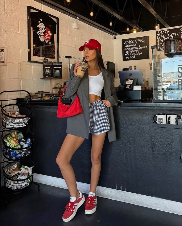 Woman in casual outfit with red cap and bag drinks iced coffee at a trendy café.