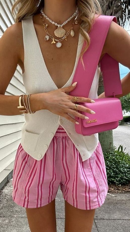 Woman in a white vest, pink-striped shorts, and pink bag, wearing seashell necklaces and bracelets.