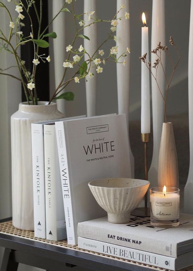 Stylish home decor with white books, vases, and candles on a shelf, creating a calming and elegant ambiance.
