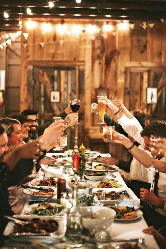 Group of people raising glasses in a rustic setting, enjoying a festive dinner under string lights.