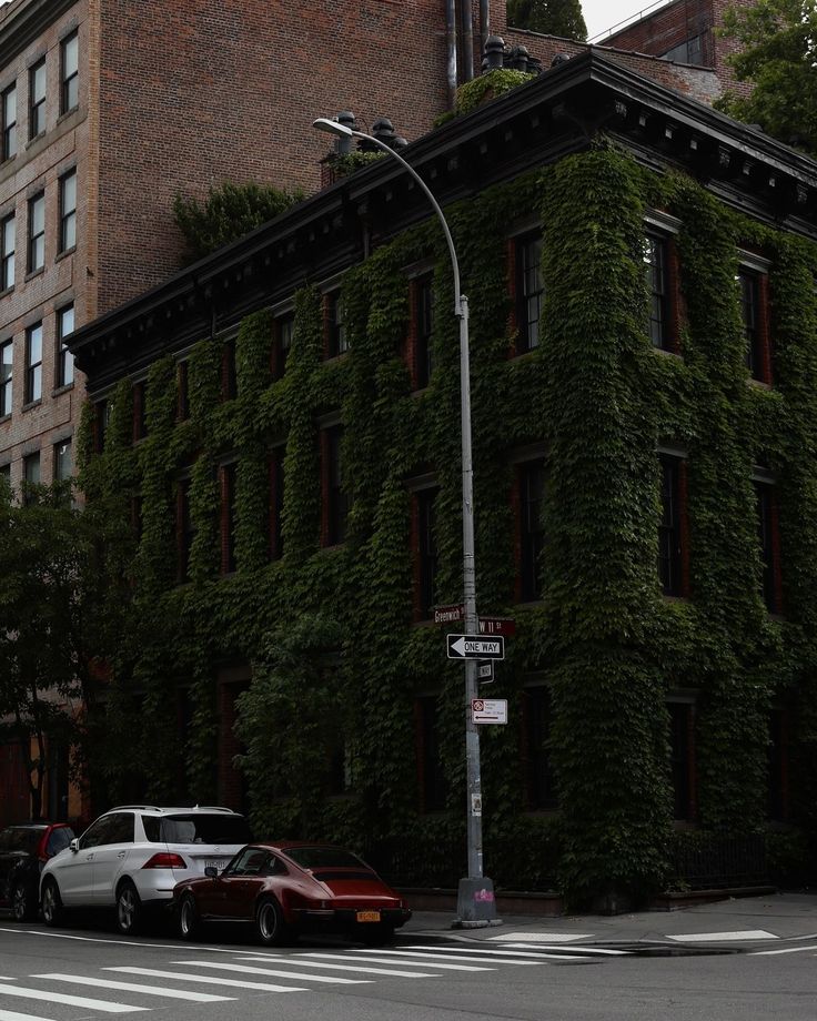 Ivy-covered building on Greenwich Street corner with classic cars parked in front, under an overcast sky.