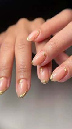 Elegant hands with nude nails featuring gold accents, showcasing a chic and stylish manicure design.