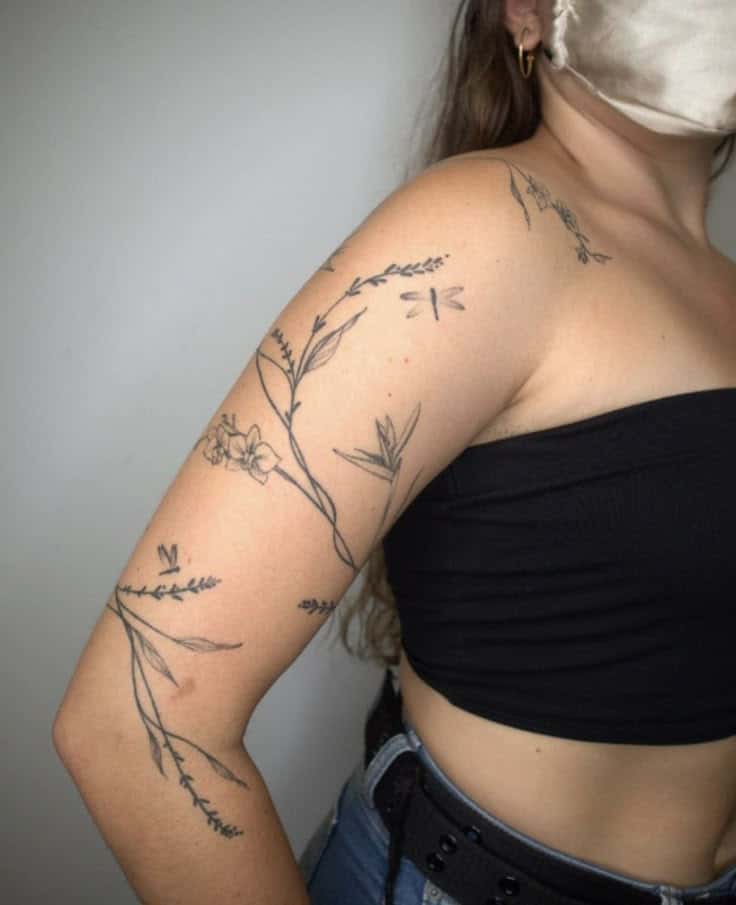 Arm with elegant floral tattoos, including delicate branches and leaves, on a person wearing a black top.