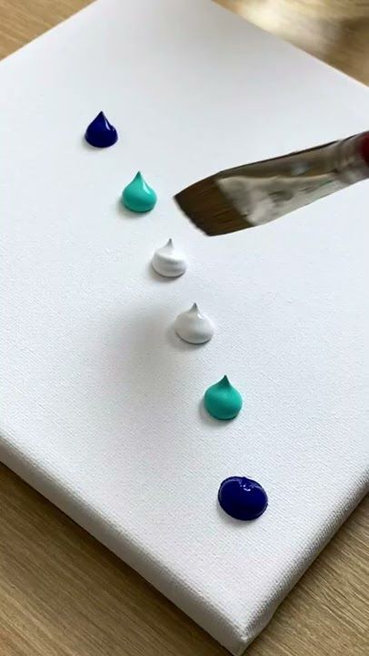 Palette knife spreading colorful paint drops on a white canvas for an abstract art project.