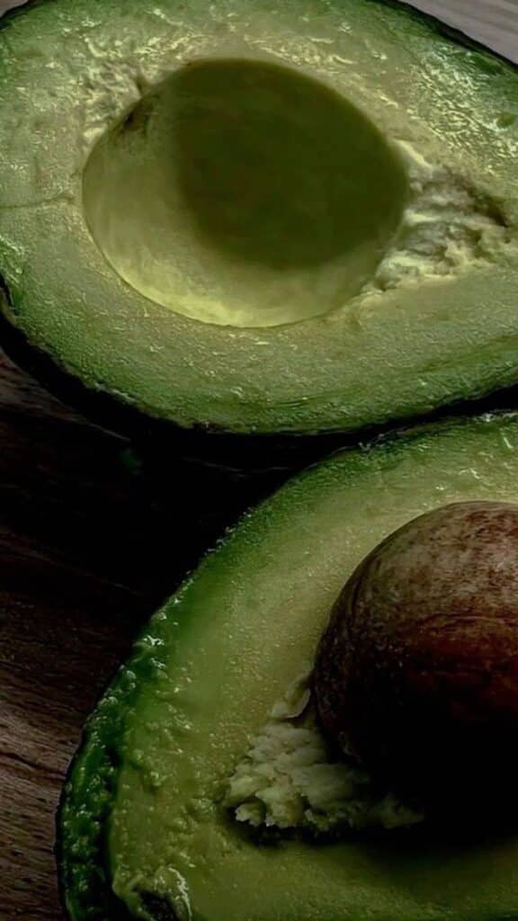 Close-up of a ripe avocado sliced in half, showcasing the seed and creamy texture on a wooden surface.