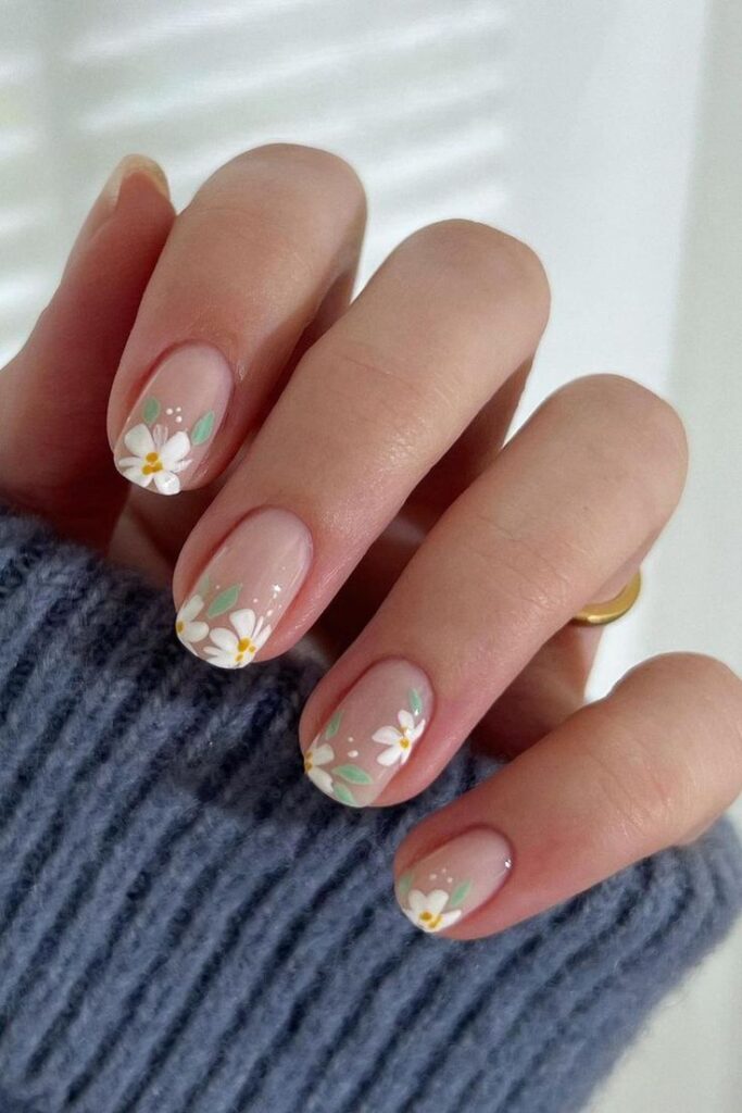 Pastel floral nail art with daisy designs on natural nails. Cozy sweater sleeve in the background for a chic look.
