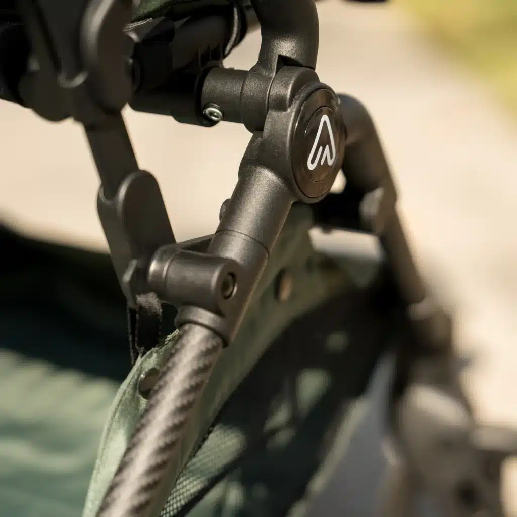 Close-up of a stroller frame with a logo, featuring sturdy metal and fabric components. Ideal for outdoor use.