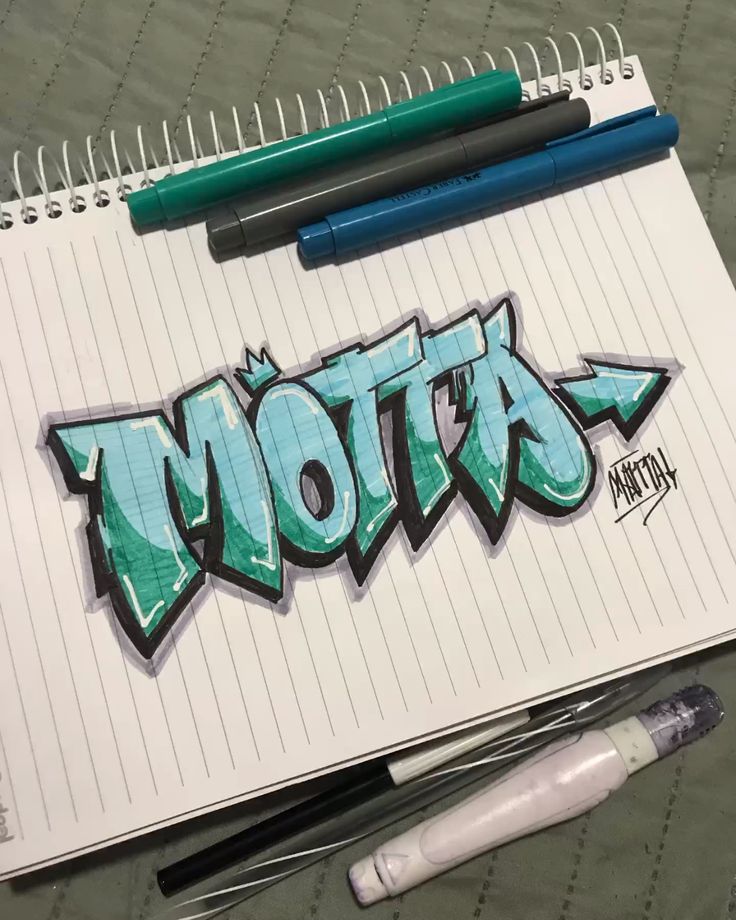 Graffiti-style Motta text on notebook page with markers and pens nearby for artistic inspiration.