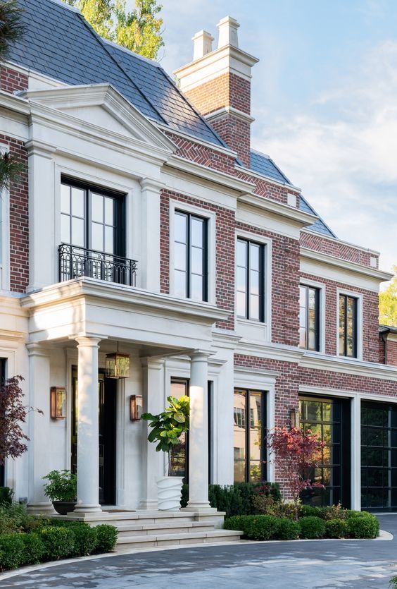 Elegant red-brick mansion with white columns and manicured shrubs on a sunny day.