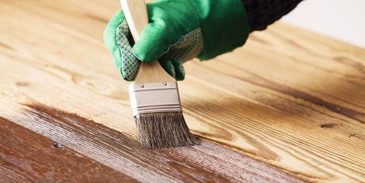 Gloved hand painting wood with a brush for a smooth finish and enhanced durability.