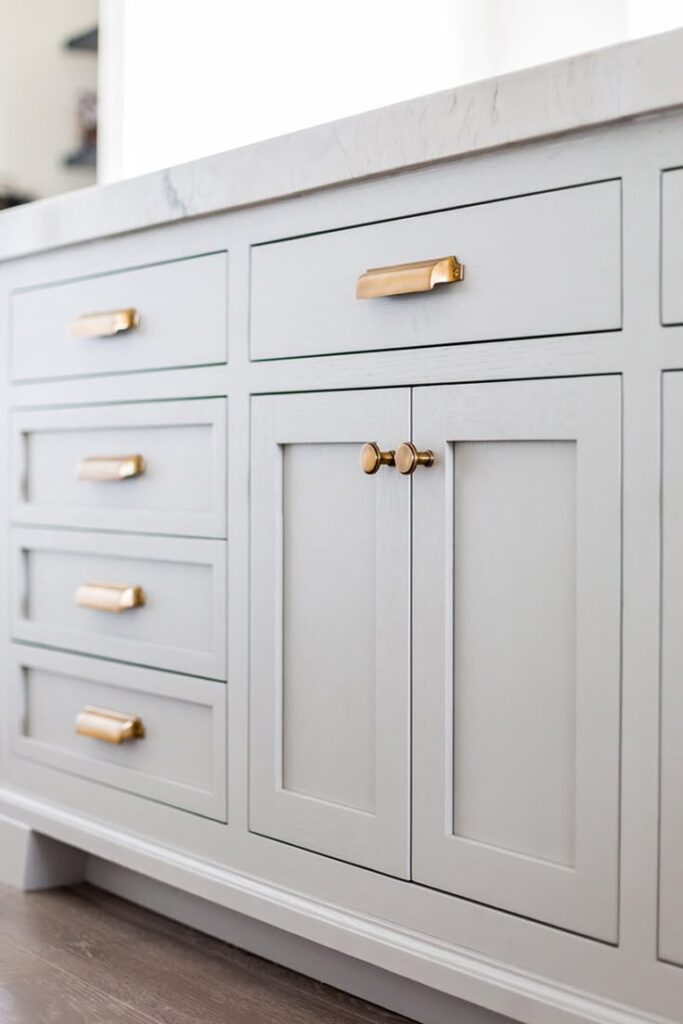 White kitchen cabinetry with gold handles and knobs, featuring a marble countertop. Modern and elegant kitchen design.