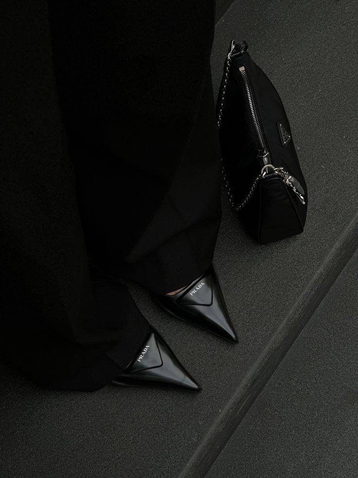 Black pointed shoes and matching handbag on dark steps, stylish elegance.
