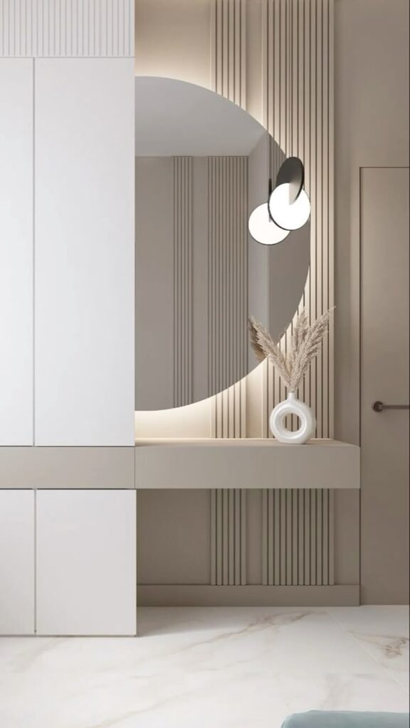 Modern minimalist hallway with round mirror, pampas grass vase, and elegant lighting.