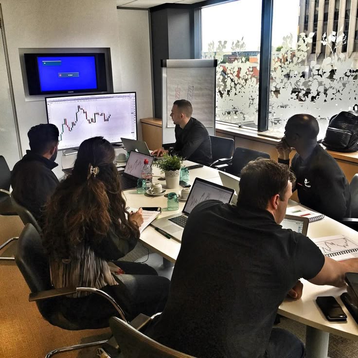 Team analyzing financial charts on laptops in a meeting room, discussing market trends.