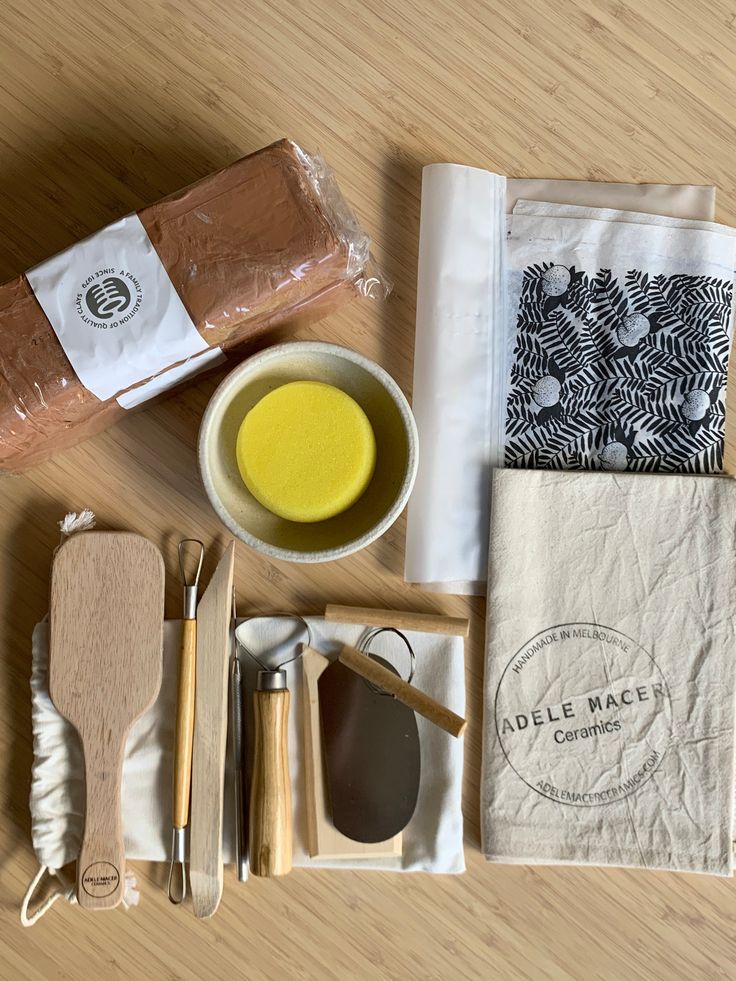 Pottery tools and materials: clay block, foam sponge, wooden tools, linen cloth, and ceramic fabric on a wooden surface.