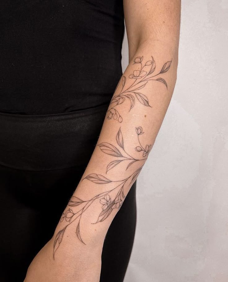 Arm with delicate floral tattoo design on forearm, featuring leaves and small flowers in elegant line art.