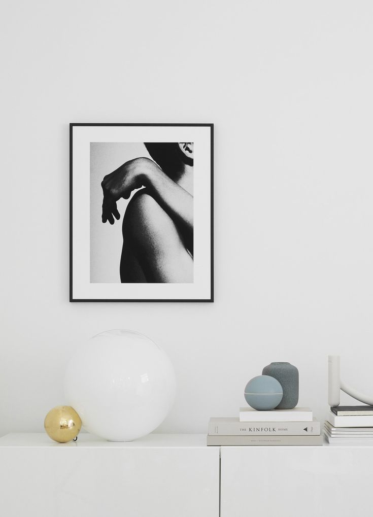 Framed black-and-white photograph on minimalist white wall, with books and decor on a modern sideboard.