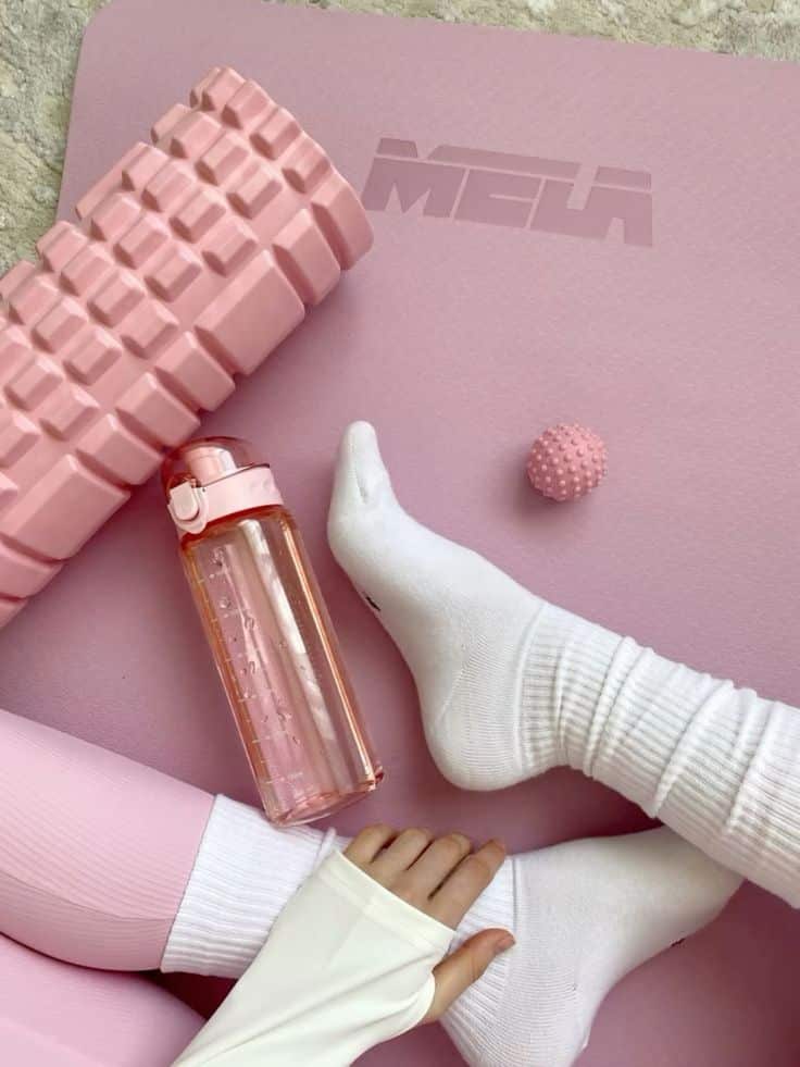 Pink yoga mat with foam roller, water bottle, and socks. Ideal for home workout or yoga session.