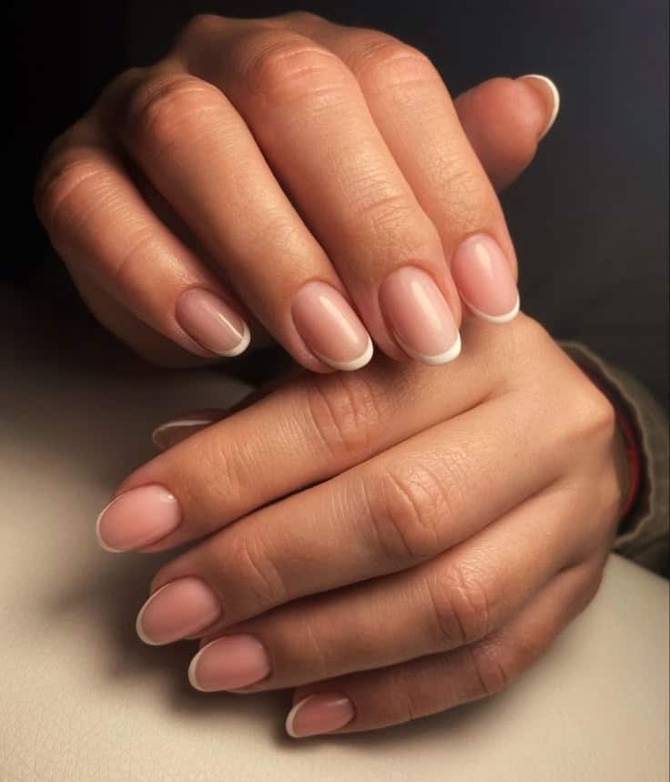 Close-up of manicured hands with elegant French tips, showcasing professional nail art and neat cuticles.