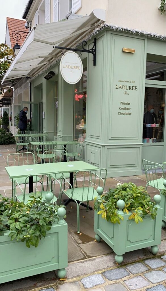 Outdoor seating area of a pastel green patisserie with plants and signage reading Ladurée Paris.