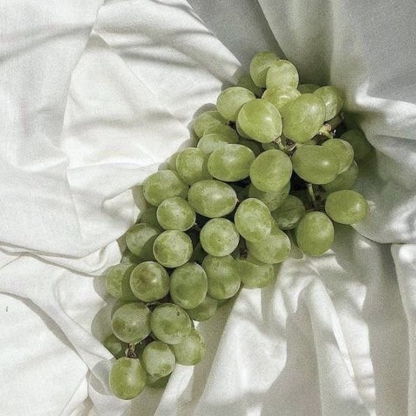 Cluster of fresh green grapes resting on white fabric, capturing natural textures and shadows.