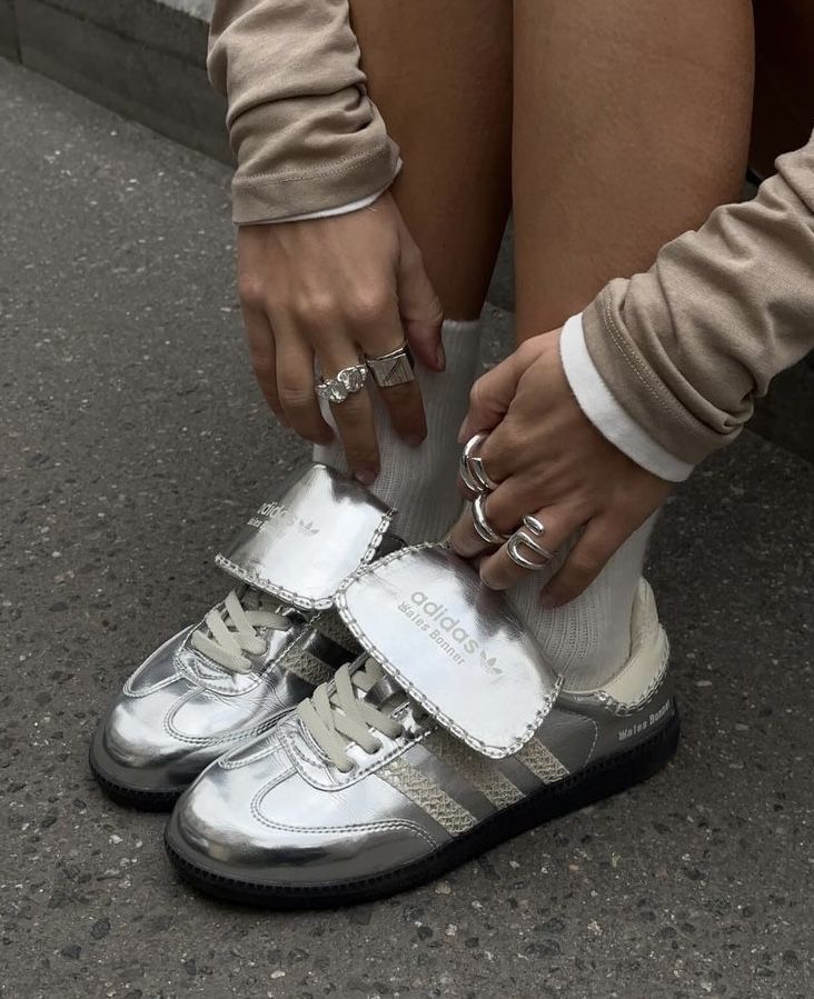 Silver Adidas sneakers with reflective finish and white socks, worn by person with stylish rings. Urban fashion footwear.