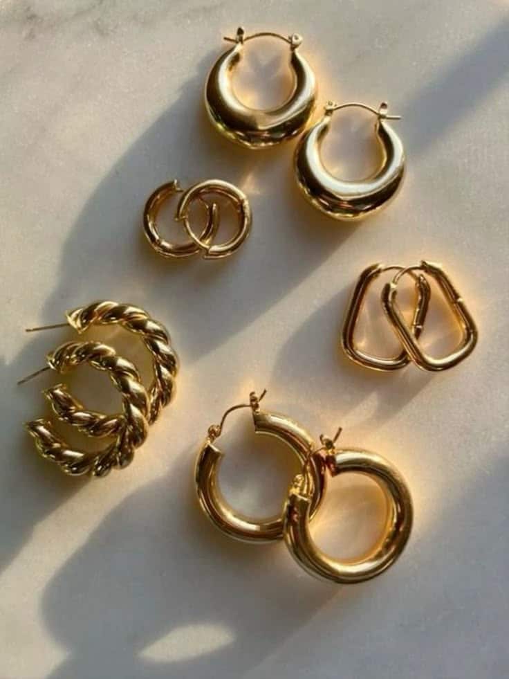 Collection of gold hoop earrings of various designs on a white background, illuminated by soft sunlight.