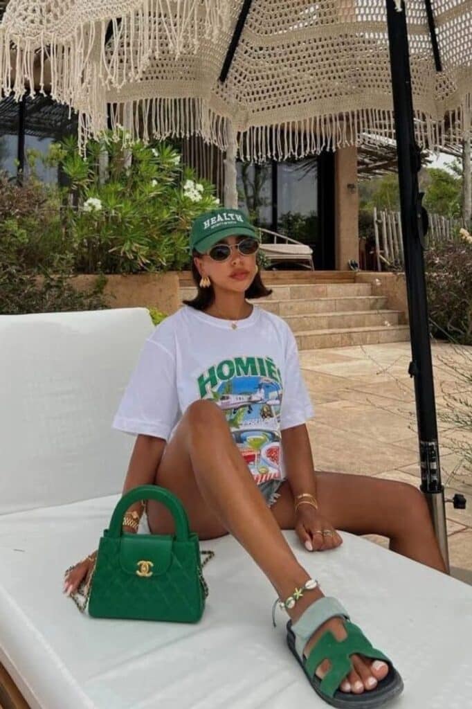Stylish woman relaxing under umbrella in casual outfit with green accessories at sunny outdoor setting. Fashion Summer Outfits