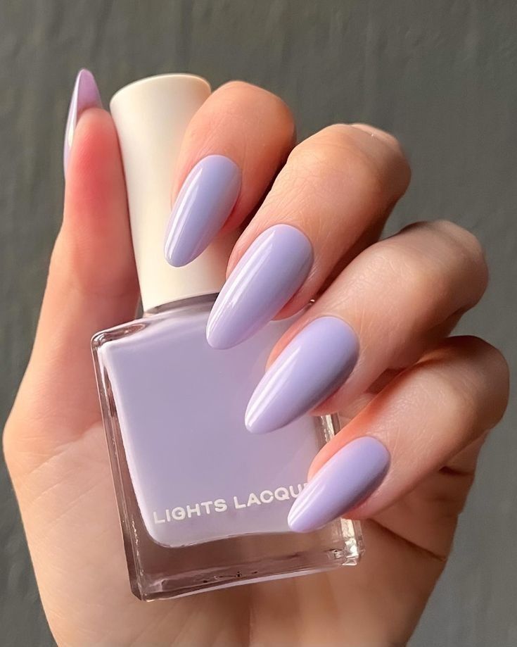 Pastel lavender nails with a matching polish bottle on a hand, showcasing elegant and stylish nail design.