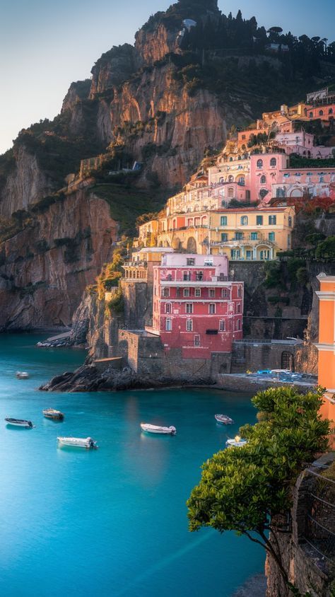 Colorful cliffside buildings by the sea in Positano, Italy, with boats on turquoise water and a rocky hillside.