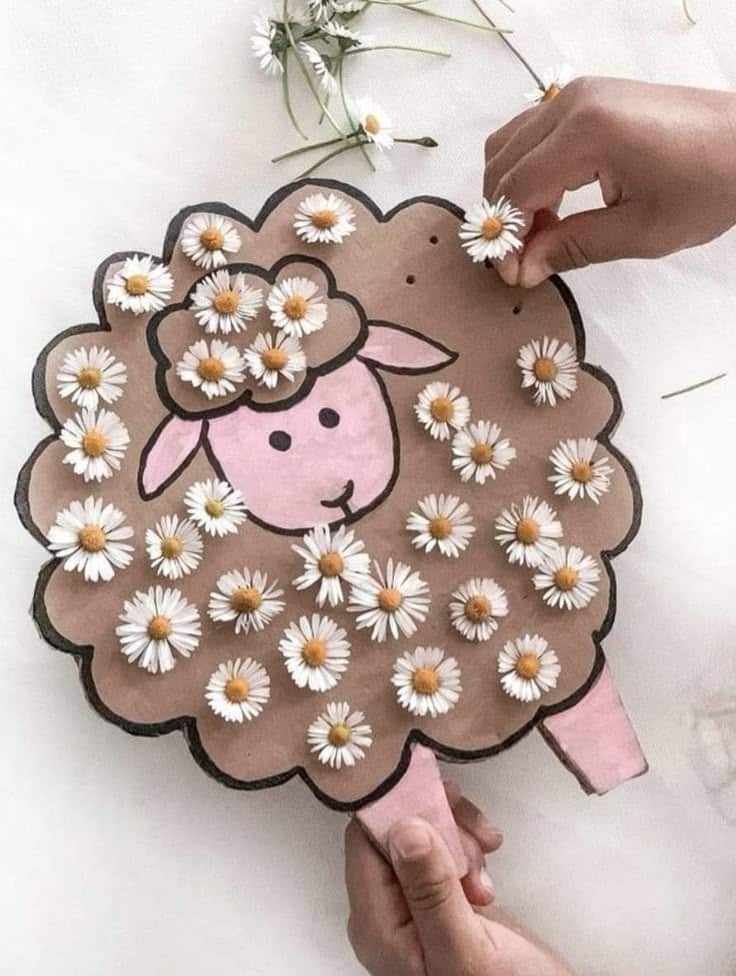 Sheep craft decorated with daisies, hands adding flowers, creative DIY project with handmade sheep art.