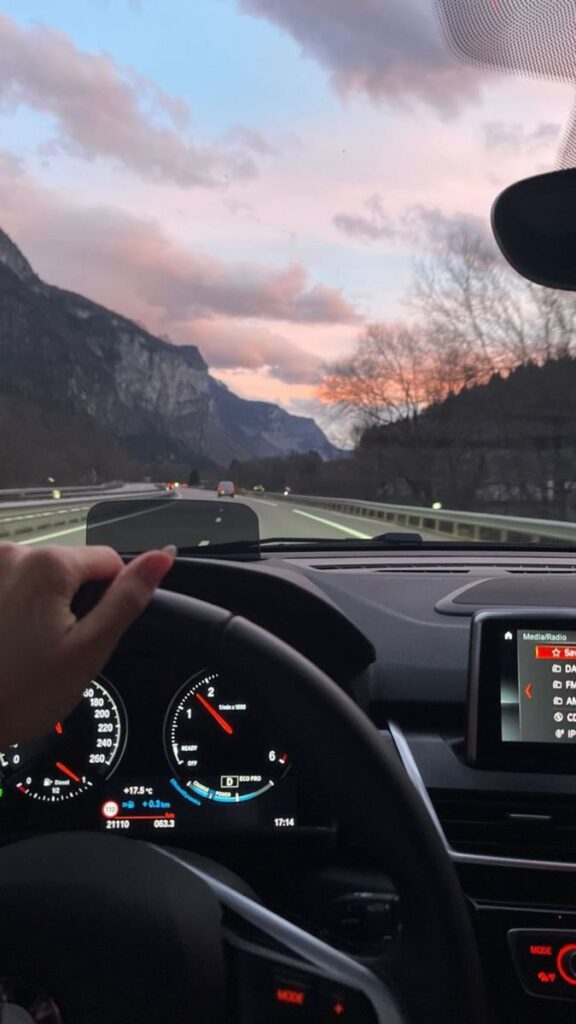 Driving through scenic mountain road at sunset, dashboard view with pink sky and distant peaks.