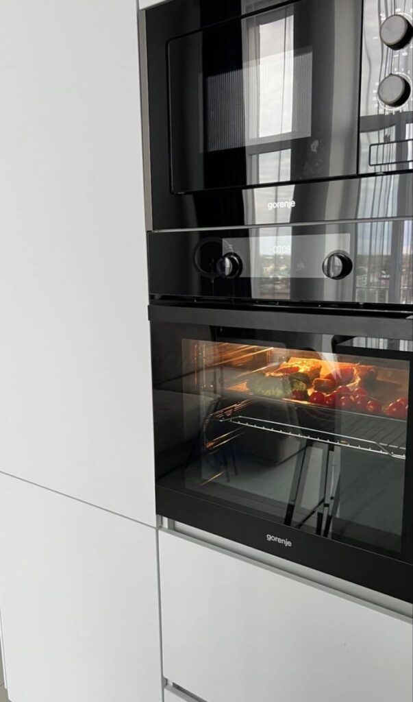 Modern black oven with chicken and vegetables cooking inside.