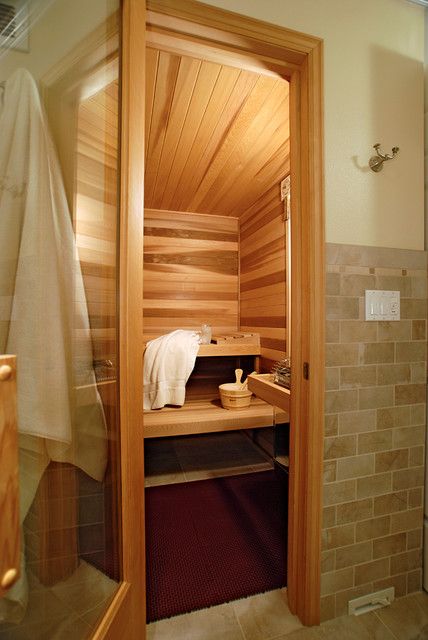 Wooden sauna with towel and water bucket, featuring warm lighting and stone tile exterior for a cozy, relaxing atmosphere.