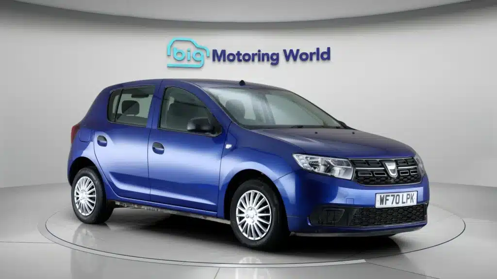 Blue hatchback car in showroom, displayed at Big Motoring World, angled view with branding and license plate.