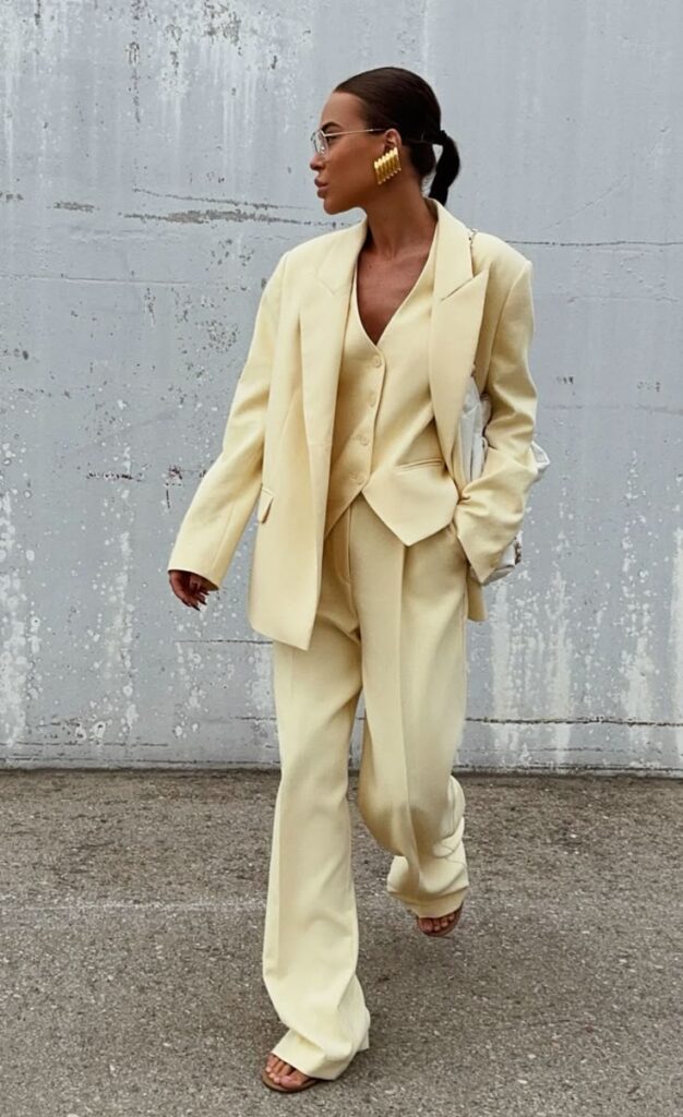 Fashionable woman wearing a cream suit and oversized blazer, accessorized with bold earrings and sunglasses.