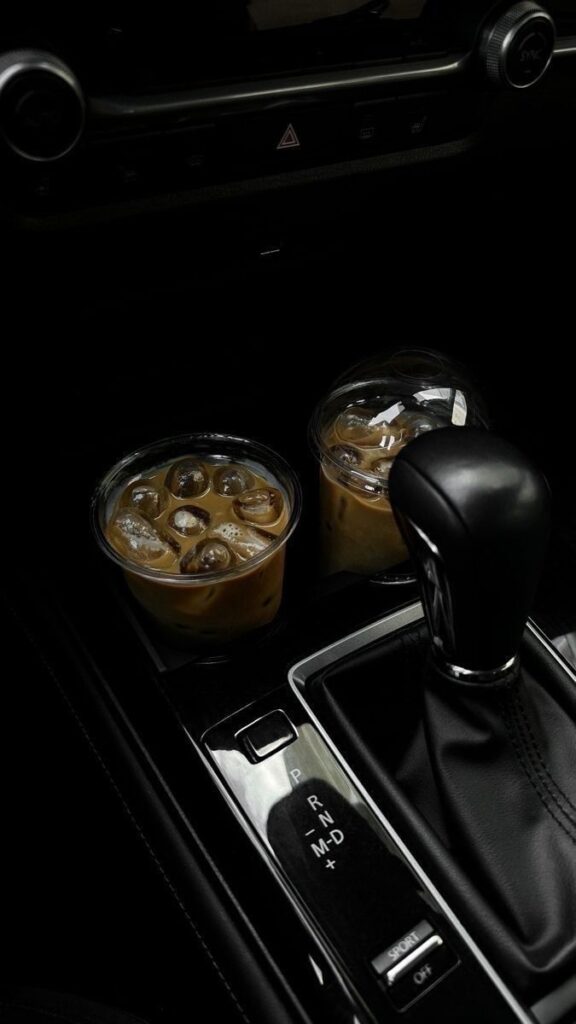 Iced coffee cups in a car cup holder next to a black gear shift, perfect for a road trip refreshment.