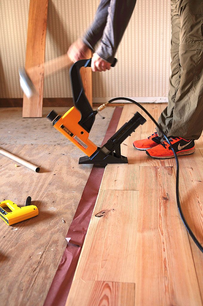 Person using a flooring nailer to install hardwood flooring in a room.