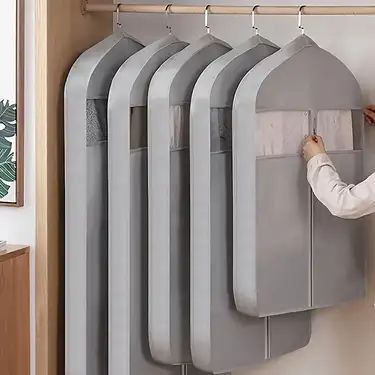 Five grey garment bags hanging in a closet, person adjusting one. Ideal for organized closet storage.