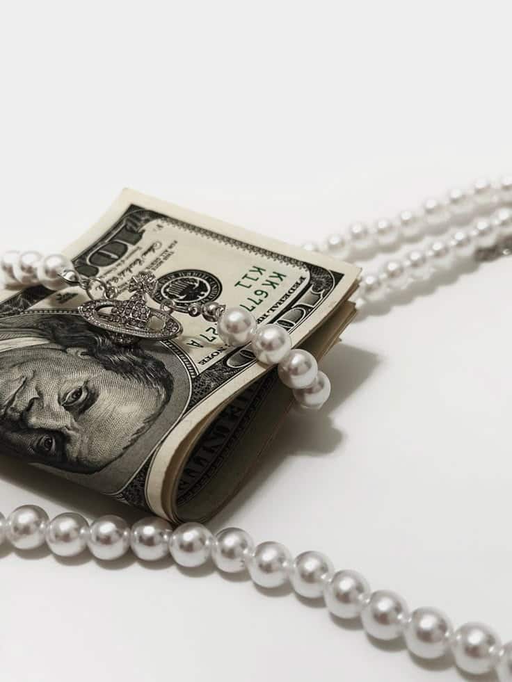 Stack of hundred-dollar bills wrapped in a pearl necklace on a white background.