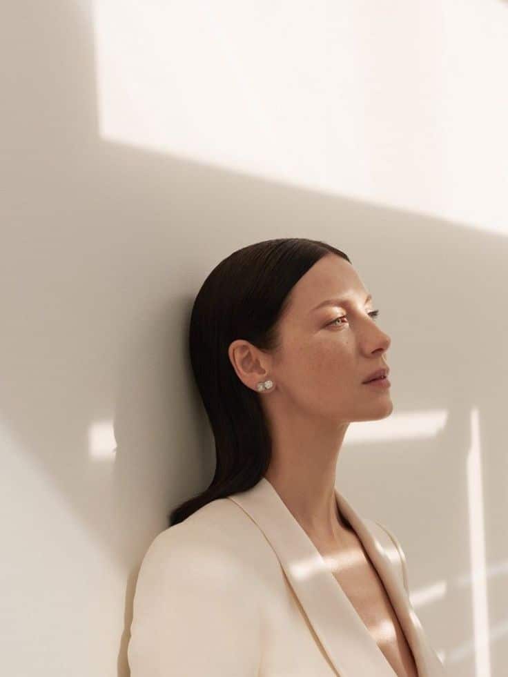 Elegant woman in a cream blazer, with light casting soft shadows on the wall, exudes sophistication and poise.