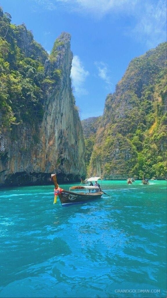 A longtail boat floats on turquoise waters between limestone cliffs under a blue sky.