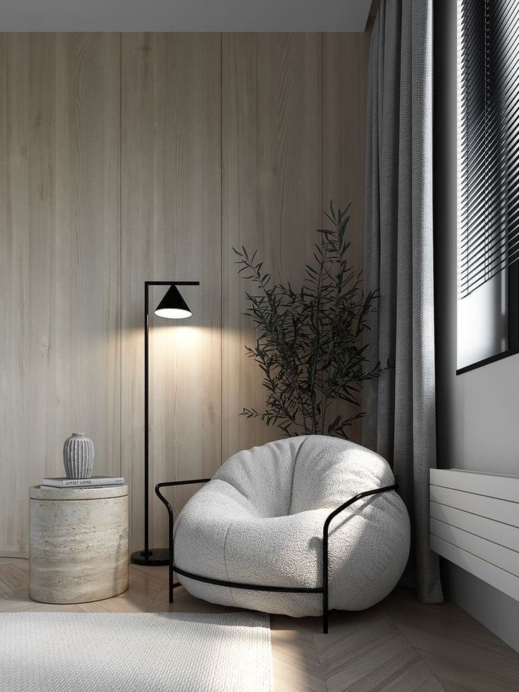 Cozy living room with a plush armchair, side table, floor lamp, and a plant against a wooden paneled wall.
