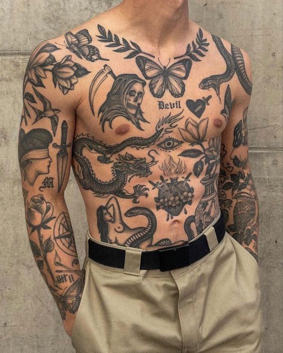 Man with intricate chest and arm tattoos, featuring a dragon, skull, butterfly, and various symbols, wearing khaki pants.